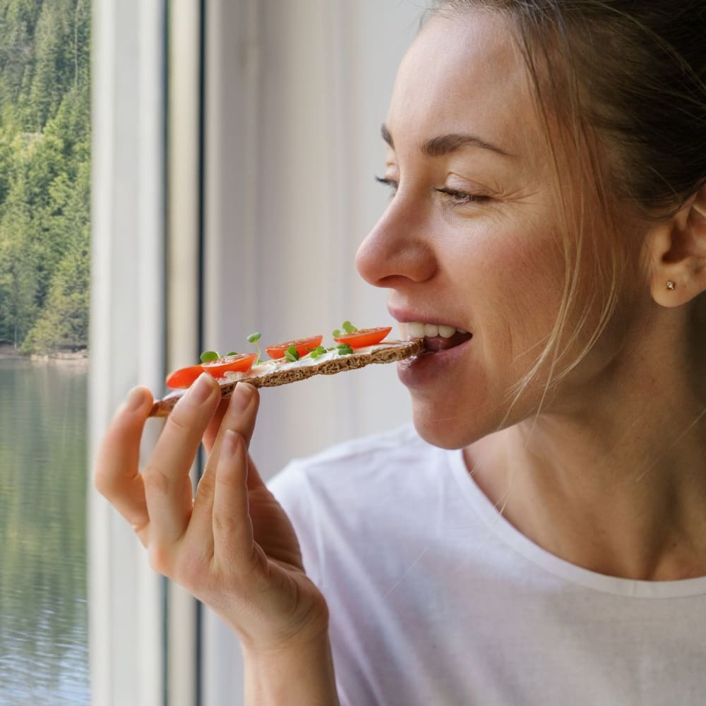 Frau beißt in ein Knäckebrot mit Microgreens und Tomaten