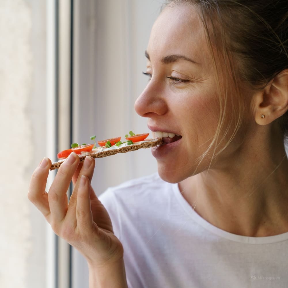 Frau beißt in ein Knäckebrot mit Microgreens  und Tomaten